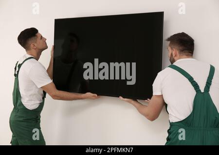 Tecnici professionisti che installano un moderno televisore a schermo piatto a parete al chiuso Foto Stock