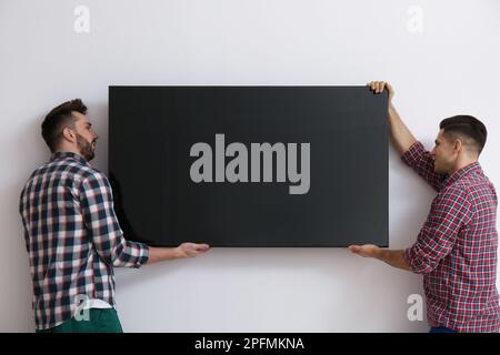 Uomini che installano una moderna TV a schermo piatto al coperto Foto Stock