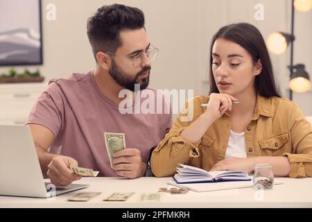 Giovane coppia che conta soldi al tavolo bianco al coperto Foto Stock