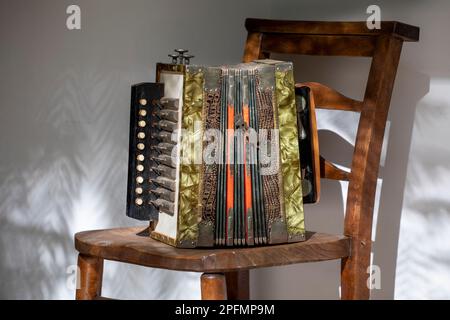 Vintage Gebrüder Ludwig, fisarmonica a bottoni su sedia di legno, all'esterno con ombre, primo piano. Foto Stock