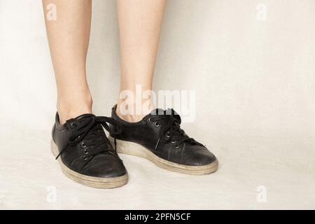 Sneaker nere ai piedi di una ragazza su un tappeto bianco, scarpe e moda Foto Stock