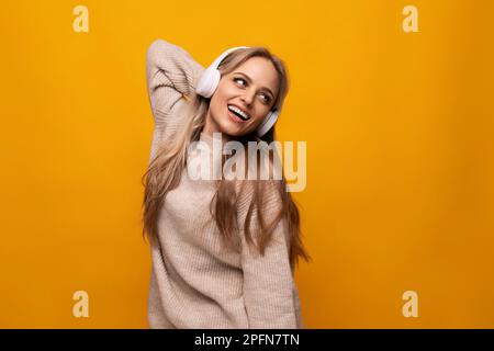 una ragazza con grandi cuffie ascolta la sua musica preferita su uno sfondo giallo Foto Stock