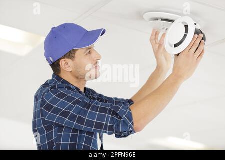 giovane elettricista che installa il rilevatore di fumo sul soffitto Foto Stock