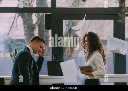Due colleghi d'affari che lottano in piedi accanto alle finestre dello spazio di lavoro co Foto Stock