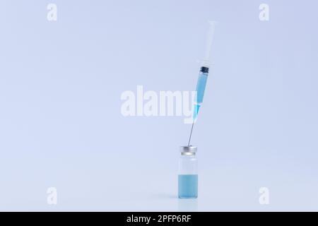 Su sfondo bianco isolato, flaconcino di vetro trasparente con vaccino blu contro i virus con siringa monouso. Lotta contro le epidemie di infezione. Co Foto Stock