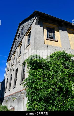 Facciata di una vecchia casa con finestre a griglia in metallo e vetri rotti in un vecchio edificio vacante Foto Stock