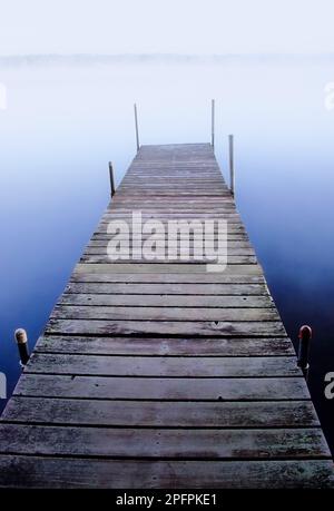 Un molo si estende in un lago di prima mattina nebbia. Foto Stock