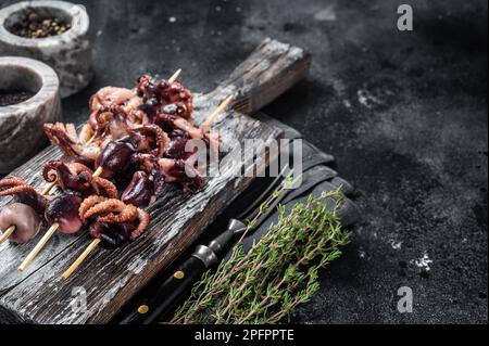 Spiedini con mini polpi alla griglia. Sfondo nero. Vista dall'alto. Spazio di copia. Foto Stock