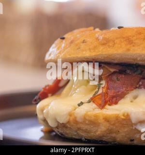 Delizioso bagel appena preparato con formaggio fuso, pancetta e basilico. Foto Stock