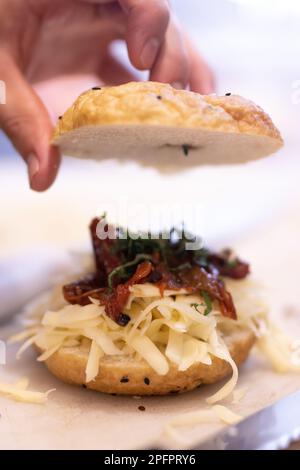 Chef prepara un bagel con formaggio, pancetta e basilico. La mano tiene il pane Foto Stock