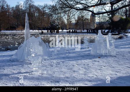 Karlsruhe, Germania - 12 febbraio 2021: Pezzi di ghiaccio ammassati in un design vicino a uno stagno con il Palazzo di Karlsruhe sullo sfondo in una giornata invernale soleggiata Foto Stock