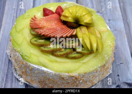 Una pan di Spagna di frutta fresca ricoperta e farcita con panna montata e noci grattugiate e ricoperta con frutta fresca di stagione con fette di AP verde e rosso Foto Stock