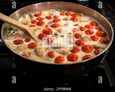 Deliziosa zuppa di cocco tailandese con pomodori in una pentola argentata con utensili di legno. Foto Stock