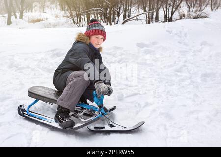 In inverno, un ragazzo guida uno scooter da neve da una montagna nella neve Foto Stock