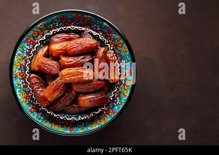 Datteri secchi in ciotola su sfondo scuro. Ciotola di date snocciolate. Cibo per Ramadan. Vista dall'alto. Spazio di copia Foto Stock
