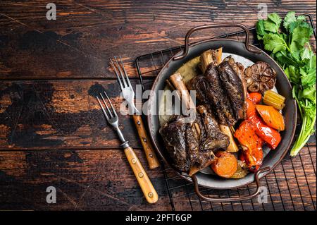 Agnelli brasati fatti in casa con salsa ed erbe in un vassoio di acciaio Sfondo di legno. Vista dall'alto. Spazio di copia. Foto Stock