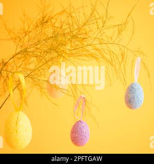 Multicolori uova di pasqua appese al ramo, poste su uno sfondo giallo brillante Foto Stock