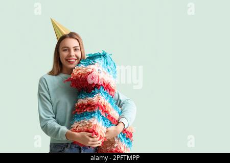 Giovane donna in cappello da festa con pinata messicana su sfondo verde Foto Stock