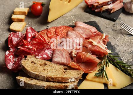 Piatto di ardesia con assortimento di gustosi salumi, pane e formaggio su sfondo grigio Foto Stock
