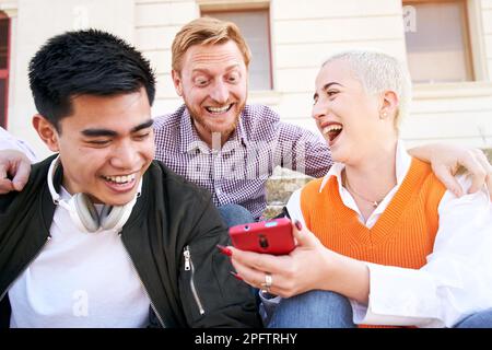 Grande risata di una donna con amici multirazziali che usano il cellulare. Persone intrattenuti con i social network. Foto Stock