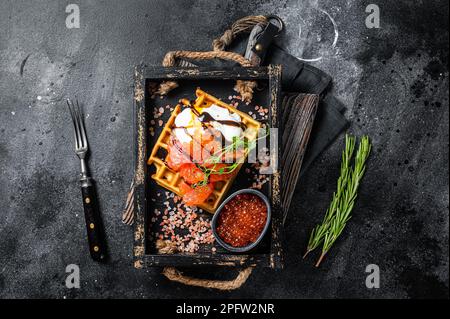 Delizioso waffle con filetto di salmone affumicato, uova in camicia e caviale rosso. Sfondo nero. Vista dall'alto. Foto Stock