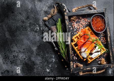 Delizioso waffle con filetto di salmone affumicato, uova in camicia e caviale rosso. Sfondo nero. Vista dall'alto. Spazio di copia. Foto Stock