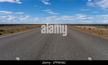 Una lunga strada diritta senza linee che attraversa il deserto di Atacama in Cile. Sole con nuvole nel cielo blu. Foto Stock