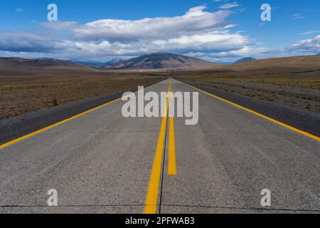 Una lunga strada diritta con linee gialle che conducono verso le montagne che attraversano il deserto di Atacama in Cile. Sole con nuvole nel cielo blu. Foto Stock