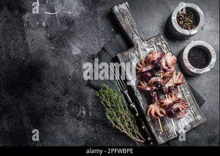 Spiedini con mini polpi alla griglia. Sfondo nero. Vista dall'alto. Spazio di copia. Foto Stock