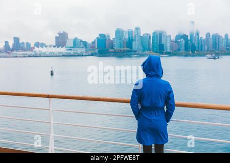 Autunno città scenario donna che cammina da sola sotto la pioggia indossando impermeabile blu in giorno umido freddo. Skyline di Vancouver, Canada. Viaggio in nave da crociera Foto Stock