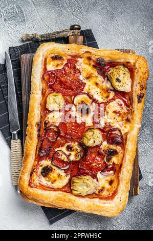 Pizza vegetariana con pasta sfoglia, carciofo, mozzarella, pomodori e formaggio. Sfondo bianco. Vista dall'alto. Foto Stock