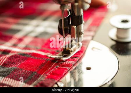 Primo piano. Una donna lavora a casa su una macchina da cucire elettrica. Cucire il tessuto su una macchina da cucire da vicino Foto Stock