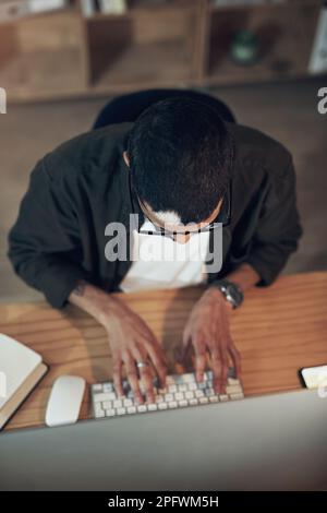 Versando ore di ricerca nel suo progetto. Ripresa ad alta angolazione di un giovane uomo d'affari che utilizza un computer durante una notte tarda in un ufficio moderno. Foto Stock