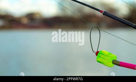 L'allarme morso si blocca su una canna da pesca contro lo sfondo dell'acqua. Canna da pesca mentre la pesca sul lago, fiume. Attrezzatura da pesca. Asta di carpa su una sta Foto Stock