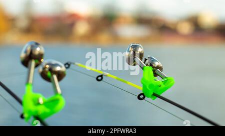 L'allarme morso si blocca sulla punta della canna da pesca contro lo sfondo dell'acqua. Canna da pesca mentre la pesca sul lago, fiume. Attrezzatura da pesca. Due Foto Stock