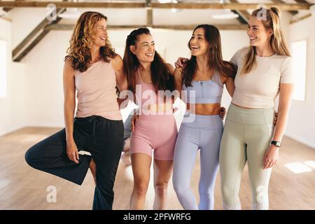 Gruppo di donne sportive sorridenti felicemente in piedi insieme in uno studio di yoga. Allegre amiche che lavorano insieme in una sala fitness. WOME Foto Stock