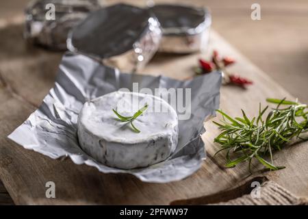 Confezioni infociate di brie con rosmarino e peperoncino su tagliere. Foto Stock