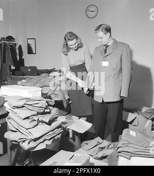 Un giovane cerca di indossare una giacca troppo grande e viene aiutato da una giovane donna a ripiegare le lunghe braccia. In scatole e a destra sono i blazer in diverse dimensioni. Svezia 1950. Kristoffersson Ref AX50 Foto Stock