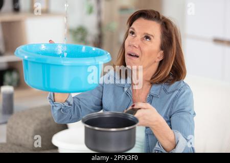 Preoccupato della donna tenendo la benna mentre le goccioline di acqua perdite dal soffitto Foto Stock