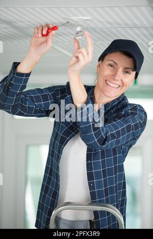 una donna che installa una nuova lampadina del faretto nel soffitto Foto Stock