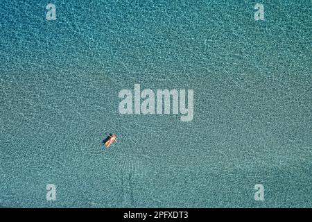 Vista aerea dall'alto verso il basso di un uomo sul materasso gonfiabile sull'acqua di mare limpida Foto Stock