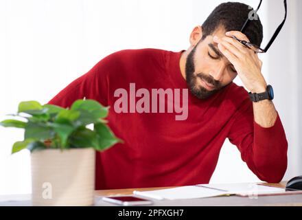 Stressato giovane seduto al banco di lavoro, toccando la testa Foto Stock