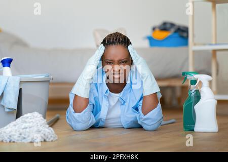 Donna nervosa nera irritata sdraiata sul pavimento mentre fa i lavori Foto Stock