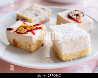 Piatto bianco pieno di dolci diversi. Gustosi dessert con farcitura, fiocchi di cocco. Foto Stock