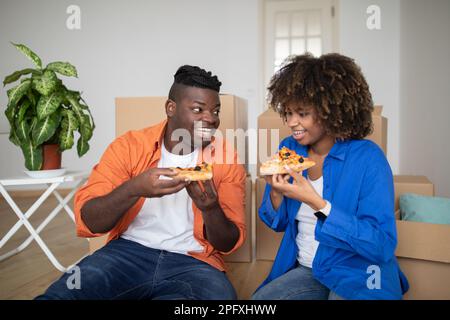 Allegra coppia nera con pausa pranzo pizza dopo il trasferimento in una nuova casa Foto Stock