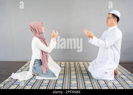 Uomo e donna musulmana che legge un libro su sfondo grigio, in uno studio sull'Islam. Mano di musulmani che pregano con sfondo interno moschea Foto Stock