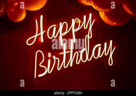 Goiania, Goias, Brasile – 18 marzo 2023: Scritto "buon compleanno" con luce al neon su sfondo rosso e con diversi palloncini intorno. Foto Stock