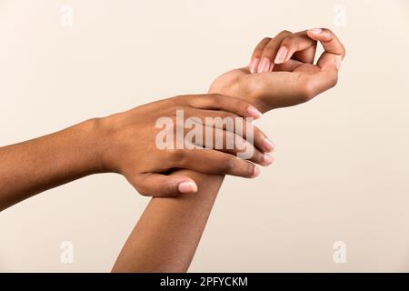 Ritaglia il polso femminile afro-americano anonimo, mentre dimostra la manicure naturale su sfondo beige Foto Stock