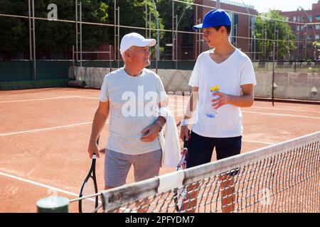 nonno e nipote parlano sul campo giocando a tennis Foto Stock