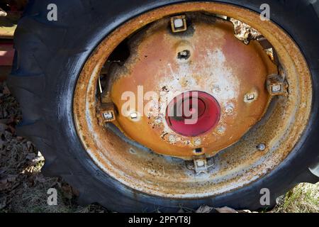 Primo piano della ruota arrugginita nera per impieghi pesanti di un vecchio trattore agricolo nel New England. Piccolo cerchio rosso al centro della ruota. Foto Stock